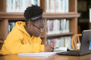 student working on assignment in the library with book notebook and laptop